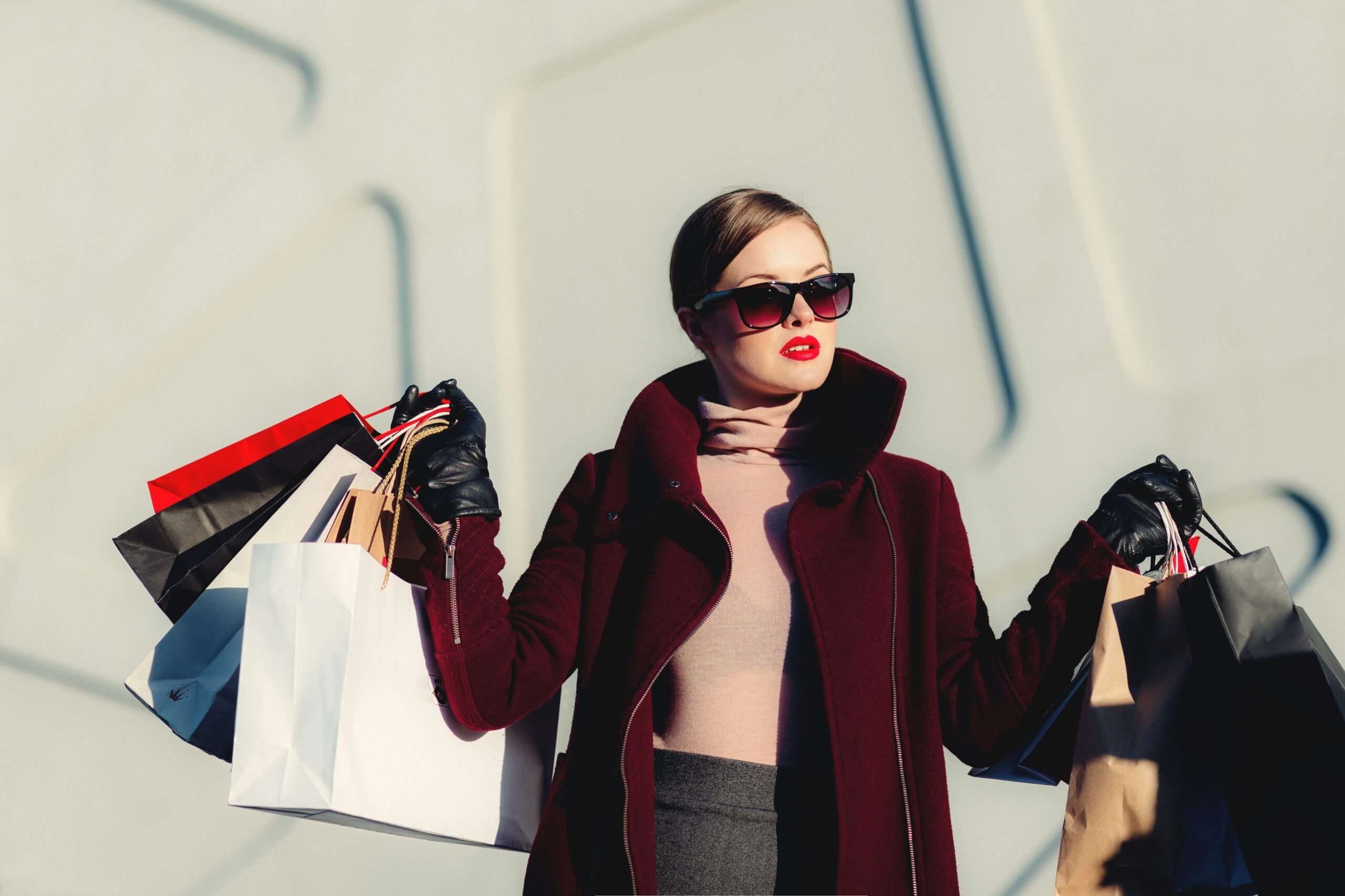 A woman in a red coat and pink top holding a large amount of shopping bags