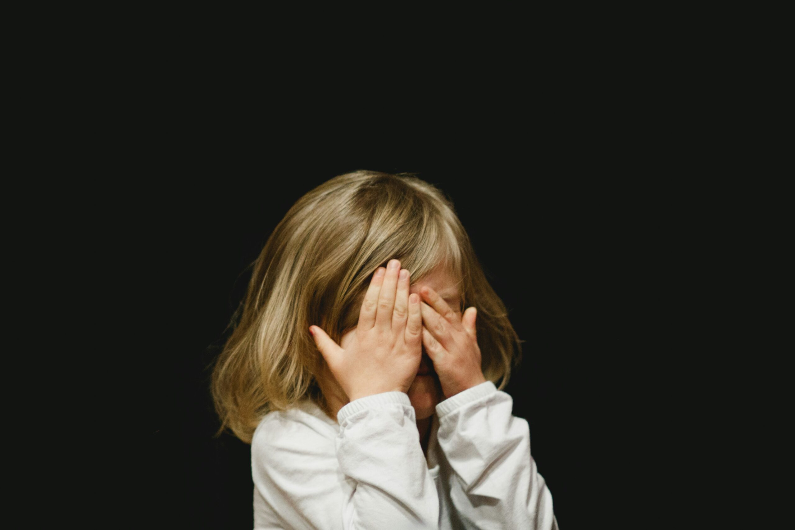 Little girl hiding her face on black background.